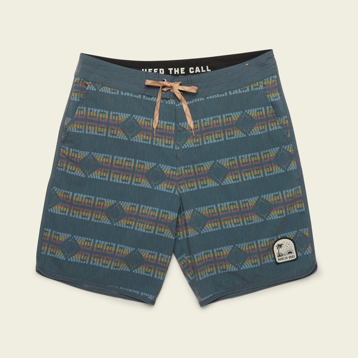 Blue patterned Bruja Boardshorts with a tan drawstring, geometric designs in muted colors, and a patch on the left leg featuring a palm tree and text—perfect stretchy boardshorts for everyday wear.