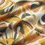 A close-up of fabric with a tropical leaf pattern in yellow, orange, and green tones. The word HOWLER is partially visible among the leaves of this lightweight cotton-poly shirt, featuring unique seasonal patterns. The material appears slightly wrinkled.