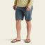 A person wearing a light yellow long-sleeve shirt, brown sandals, and Horizon Hybrid Shorts made from ripstop fabric stands against a plain, light background. The image focuses on their lower body, from torso to feet.