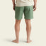 A person stands barefoot facing away, wearing green Pressure Drop Cord Shorts crafted from stretch cotton corduroy with a back pocket and a beige t-shirt, against a plain light background.