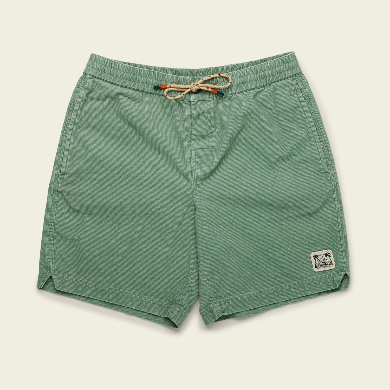 Green Pressure Drop Cord Shorts, crafted from stretch cotton corduroy, feature a palm tree patch on the lower left leg. These comfortable shorts have an elastic waistband and side pockets, set against a plain light background.