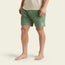 A person stands barefoot, wearing Pressure Drop Cord Shorts in green—crafted from stretch cotton corduroy for comfortable wear—and a beige t-shirt. The shorts feature a small white patch on the left leg. The background is plain and light-colored.