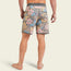 A person stands barefoot, facing away, wearing Bruja Boardshorts in pink, blue, and tan floral print with a gray waistband and trim. Made from stretchy fabric, these shorts feature draining front pockets and a back pocket with a white label.