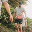 Three men walking down a lush, tropical path surrounded by green plants and palm trees. The man in front sports a patterned shirt, Buchannon Boardshorts, and a navy hat that says RAVLET. Sunlight filters through the foliage.