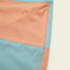 Close-up of quick drying surf shorts made from peach and light blue fabric panels with visible stitching and a vertical pocket. The image highlights the seam details and color blocking design of these boardshorts.