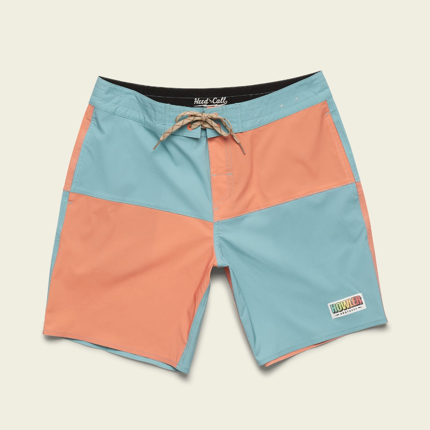 A pair of quick-drying boardshorts with light blue and coral color-blocked panels, a tan drawstring, and a small Howler patch on the lower left leg, displayed on a plain off-white background.