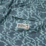Close-up of blue beach shorts with a wavy light blue pattern, featuring a flap pocket with the Howler Brothers brand label and palm tree logo. The elastic waistband is visible at the top.