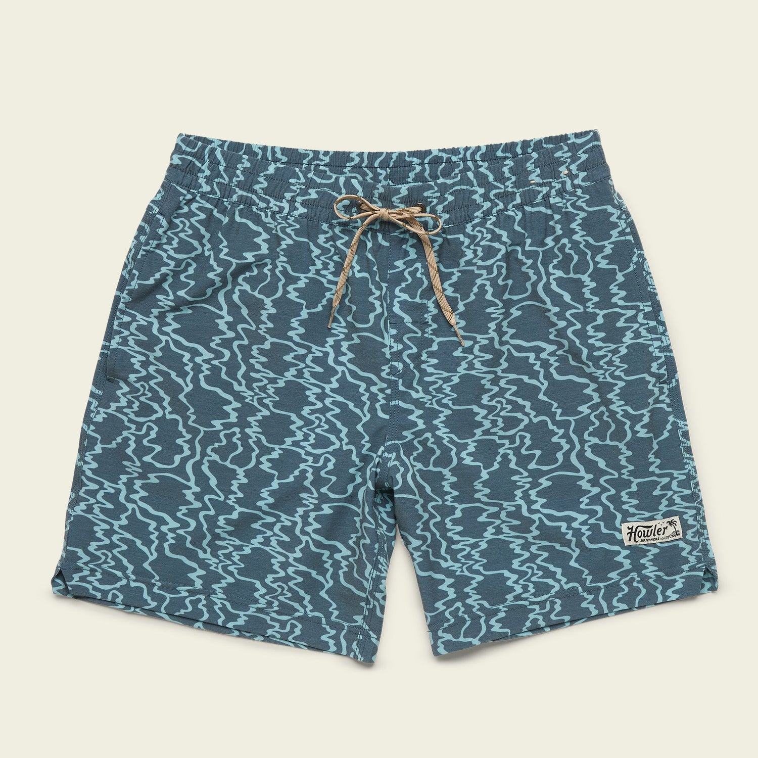 Blue beach shorts with a wavy, abstract pattern, elastic waistband, tan drawstring, and a small “Howler” patch on the lower left leg, displayed on a light beige background.
