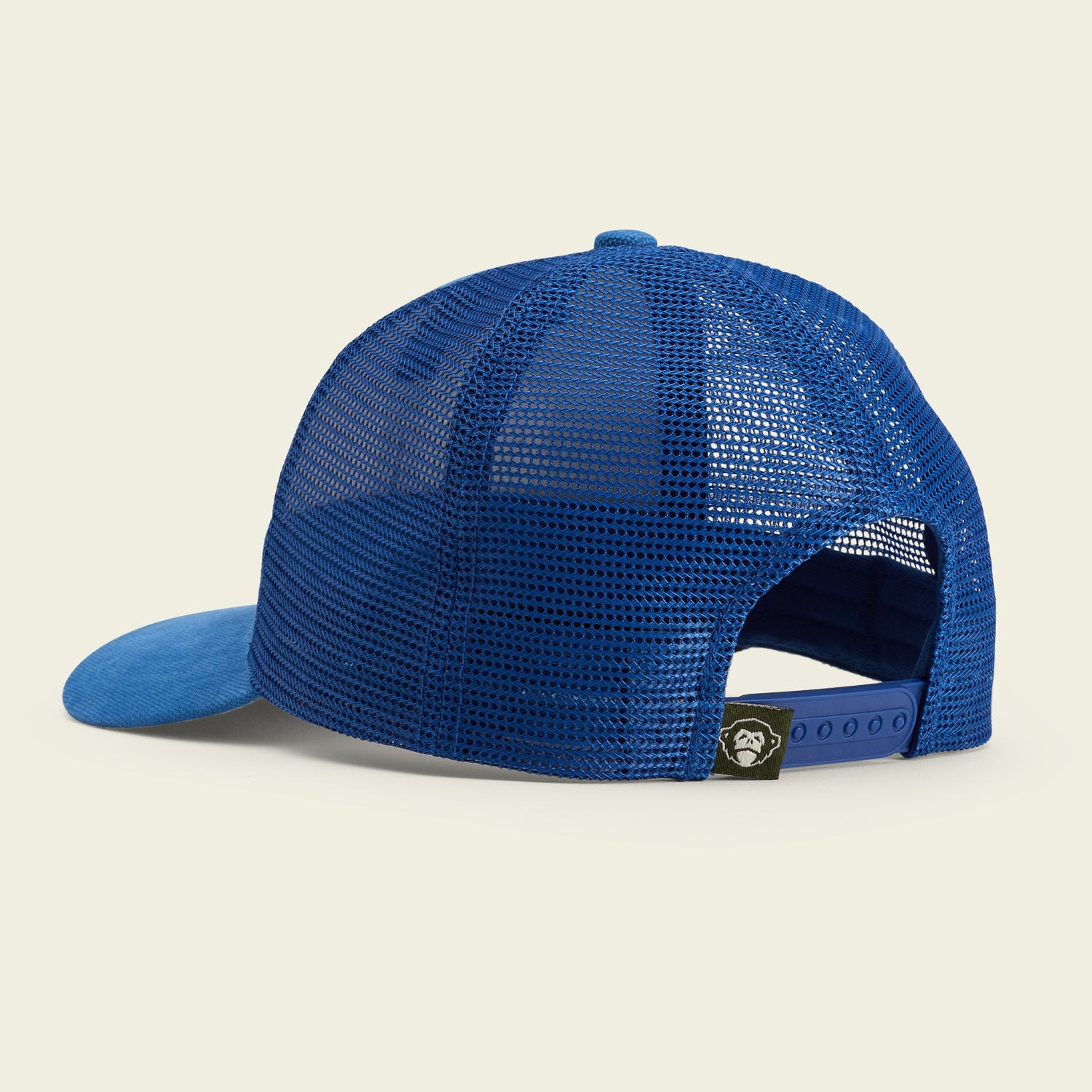 A blue mesh-back baseball cap, shown from the back angle, featuring an adjustable snapback hat closure and a small black tag with a white design near the opening.