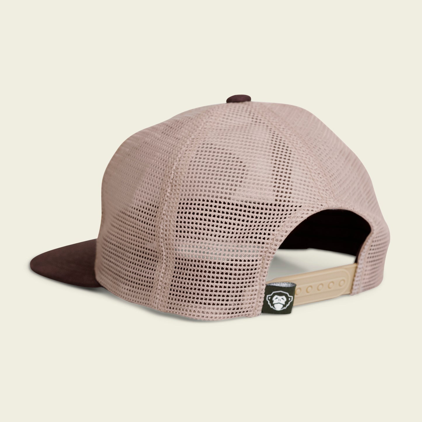 A mesh-back trucker hat shown from behind, featuring a beige adjustable snapback closure and a black tag with a white logo near the opening. The unstructured snapback has a soft crown and a darker front brim.