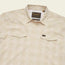 A beige plaid lightweight stretch shirt with a collar, two chest pockets with button flaps, a vented yoke for breathability, and a visible Howler Bros brand label on the inside collar.