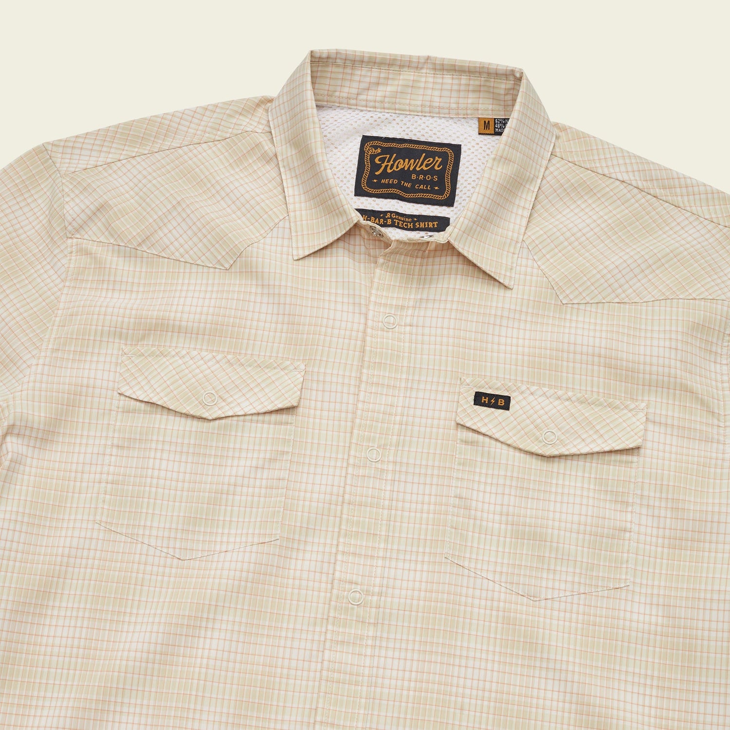 A beige plaid lightweight stretch shirt with a collar, two chest pockets with button flaps, a vented yoke for breathability, and a visible Howler Bros brand label on the inside collar.