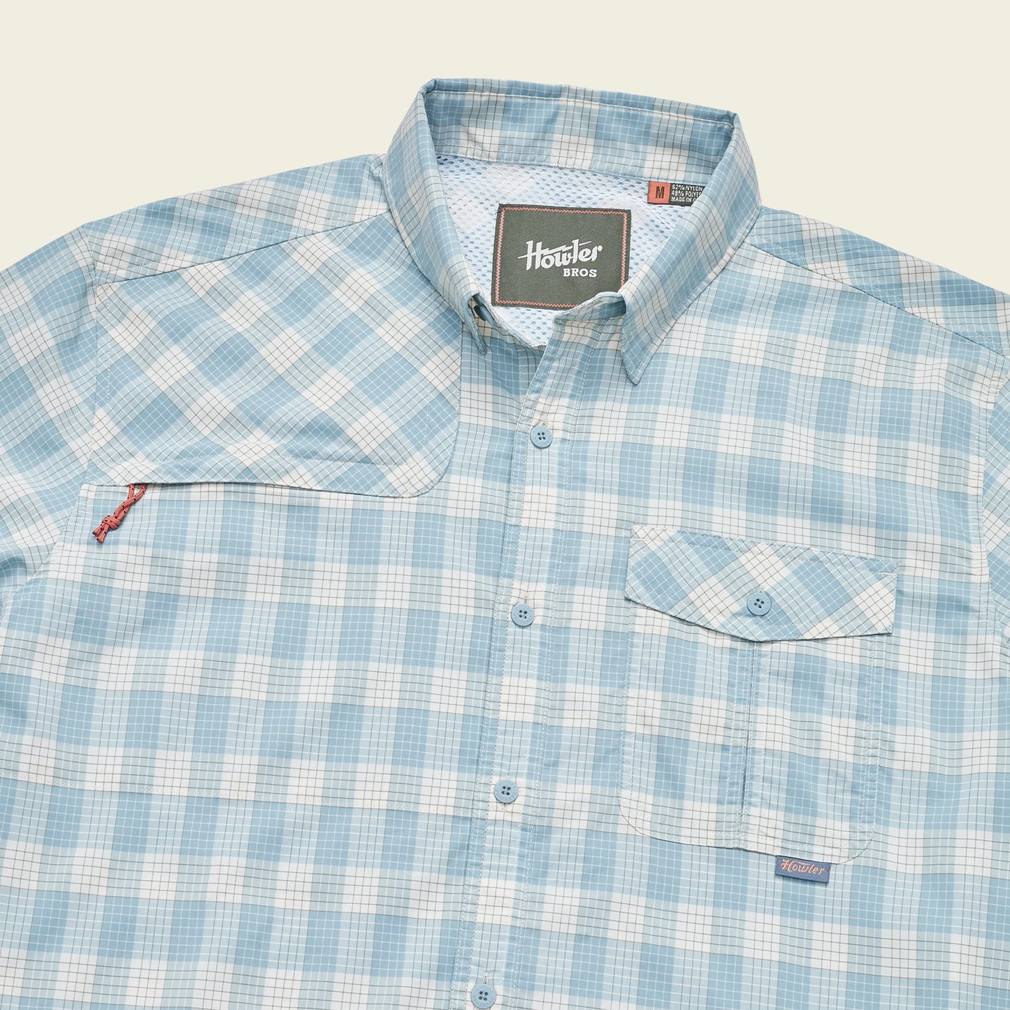 A light blue and white plaid Matagorda Shirt with a collar, front chest pocket with flap, quick drying fabric, and a Howler Bros label on the inside neck and above the pocket—perfect as your travel shirt.