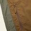 Close-up of a brown zippered pocket on the Seabreacher Jacket, with olive green fabric on the left side. The lightweight windbreaker material appears sturdy and textured, and the zipper pull is clearly visible.