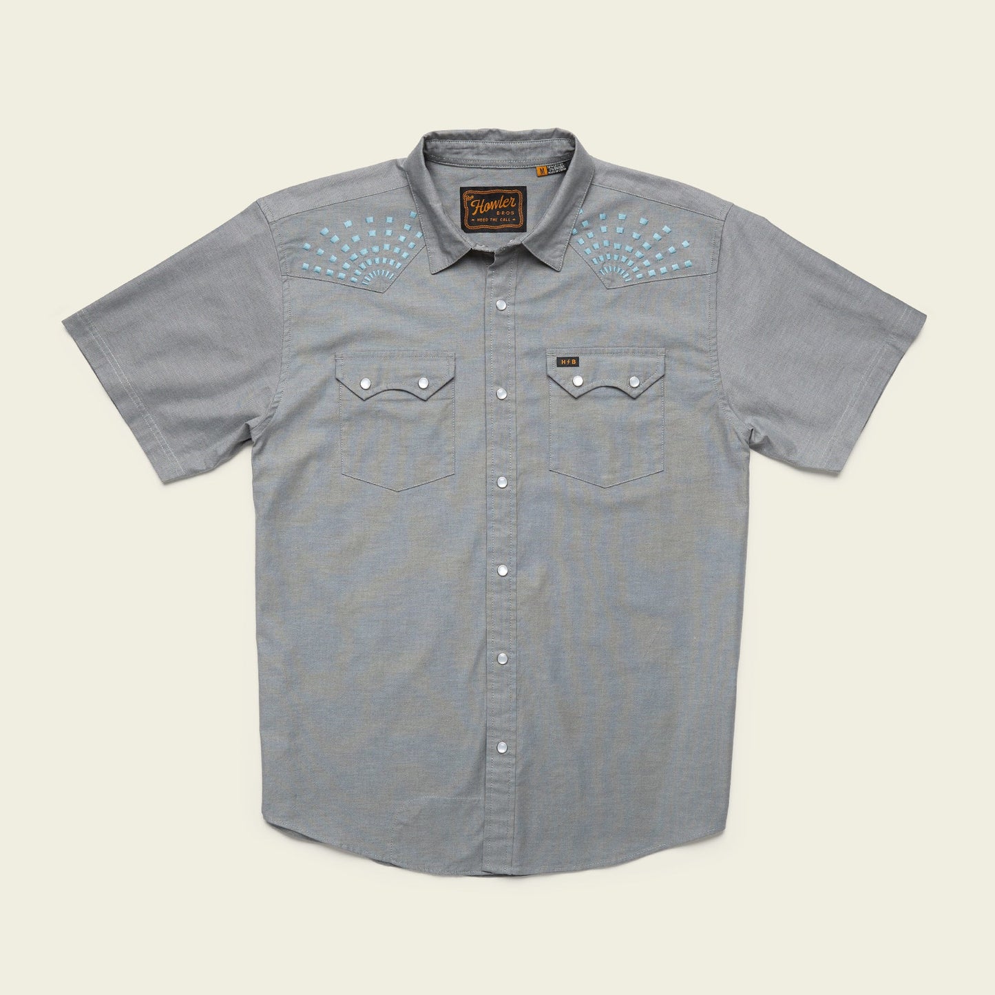Light gray Crosscut Deluxe Shortsleeve summer shirt with two chest pockets and pearl snap buttons. Features white and blue motif embroidery on the shoulders and a label above the left pocket.