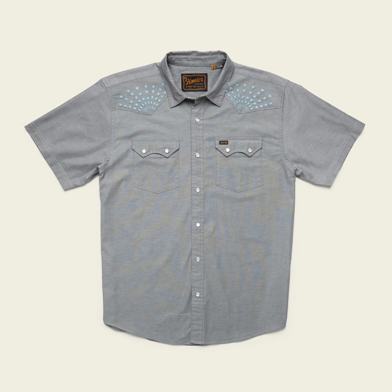 Light gray Crosscut Deluxe Shortsleeve summer shirt with two chest pockets and pearl snap buttons. Features white and blue motif embroidery on the shoulders and a label above the left pocket.