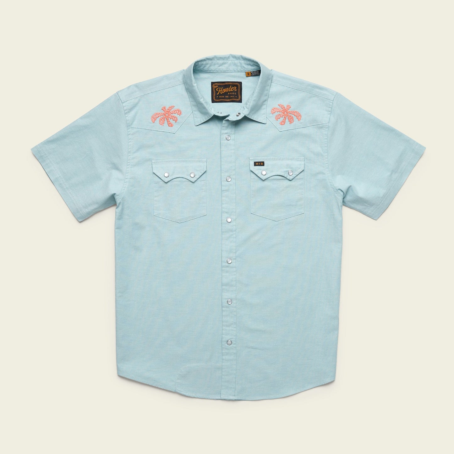 Light blue Crosscut Deluxe Shortsleeve summer shirt with two chest pockets; features pink motif embroidery of palm trees on both shoulders. Shirt is laid flat on a neutral background.