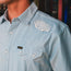 A close-up of a person wearing a light blue Crosscut Deluxe Shortsleeve with thin white stripes, motif embroidery on the shoulder, and a front pocket featuring a black and gold H+B tag.