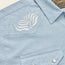 Close-up of a light blue, striped Crosscut Deluxe Shortsleeve pearl snap shirt, featuring white motif embroidery in leaf patterns on the chest.