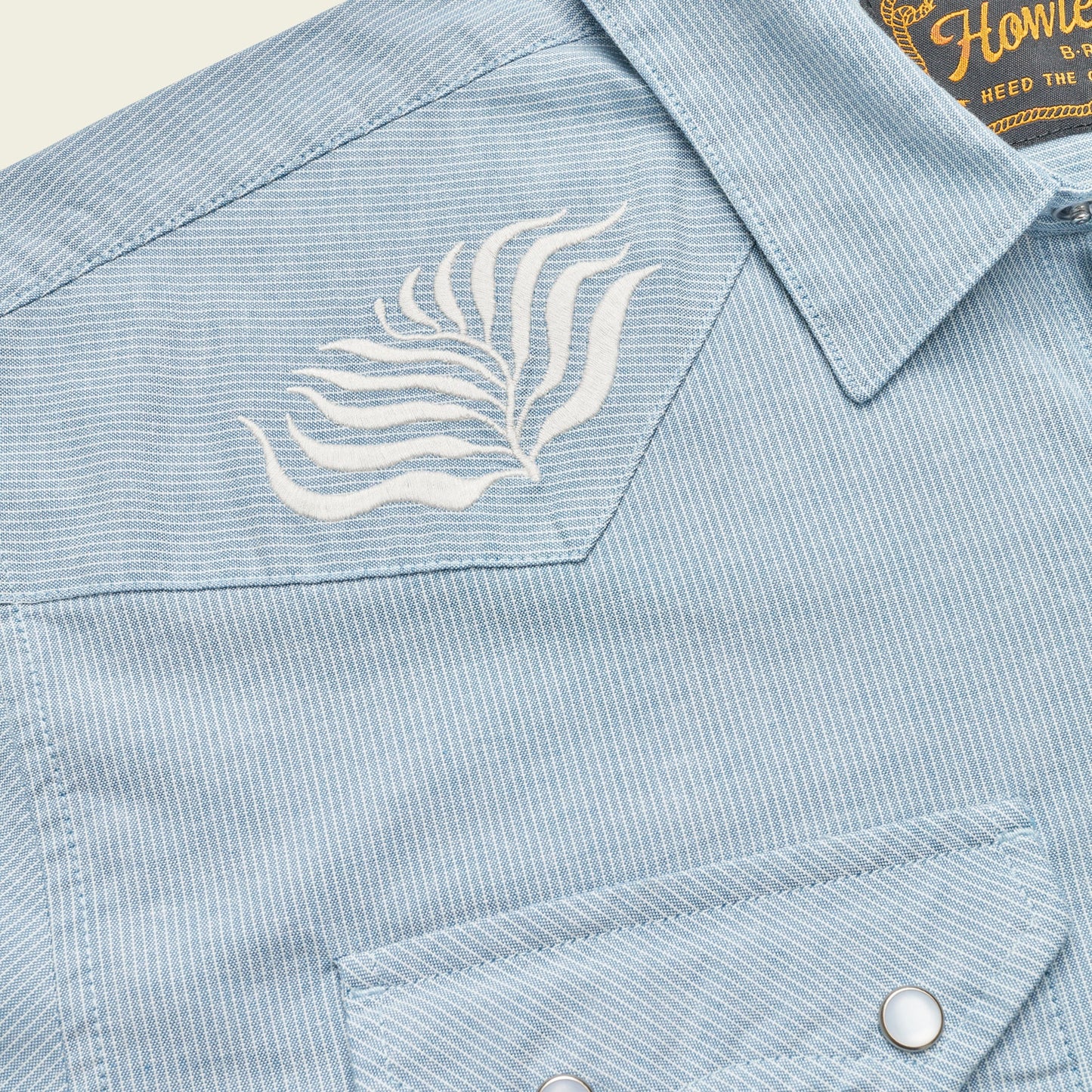 Close-up of a light blue, striped Crosscut Deluxe Shortsleeve pearl snap shirt, featuring white motif embroidery in leaf patterns on the chest.