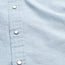 Close-up of a light blue pearl snap shirt with thin white vertical stripes and silver snap buttons along the front placket. The fabric texture, stitching details, and subtle motif embroidery are clearly visible.