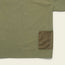 Olive green Forager Utility Shirt with a mesh brown pocket on the lower right side. Only part of this tech shirt is visible, focusing on pocket detail and fabric texture, perfect for hiking trails against a light background.
