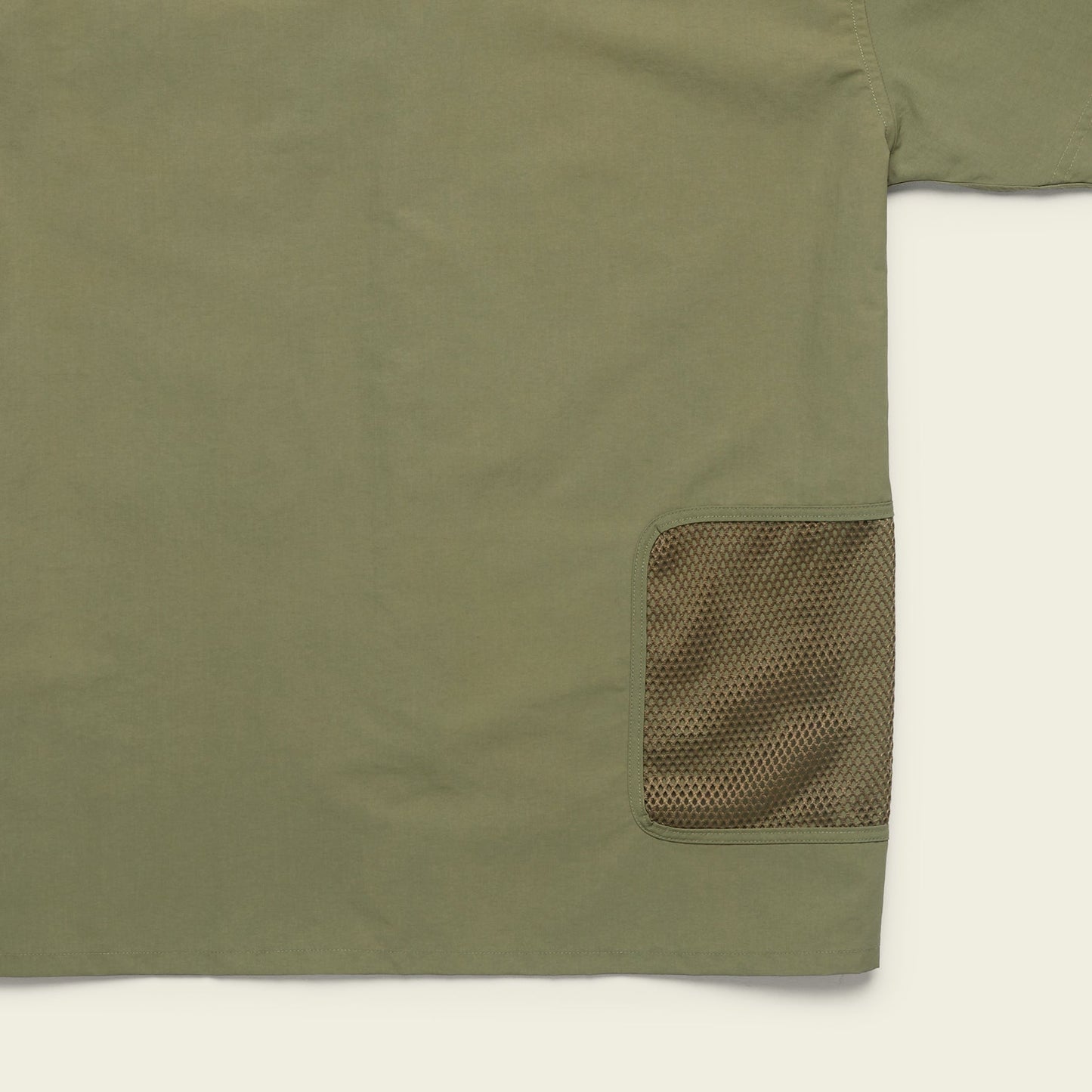 Olive green Forager Utility Shirt with a mesh brown pocket on the lower right side. Only part of this tech shirt is visible, focusing on pocket detail and fabric texture, perfect for hiking trails against a light background.