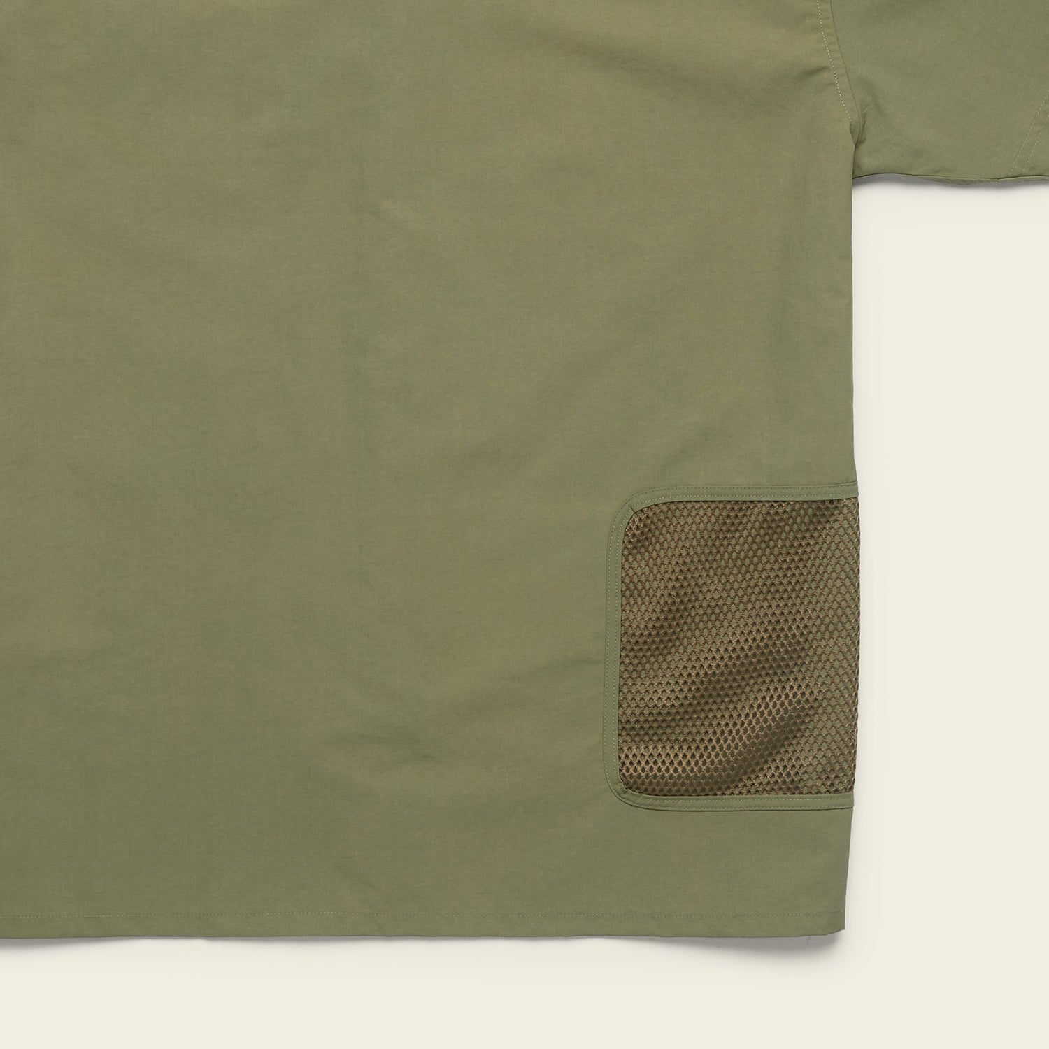 Olive green Forager Utility Shirt with a mesh brown pocket on the lower right side. Only part of this tech shirt is visible, focusing on pocket detail and fabric texture, perfect for hiking trails against a light background.
