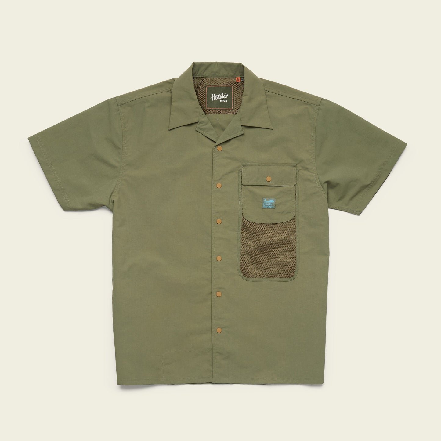 Short-sleeve olive green Forager Utility Shirt with a collar, orange buttons, and a front pocket featuring a mesh lower section and a small blue label. Perfect as a tech shirt for hiking trails. Laid flat on a light beige background.
