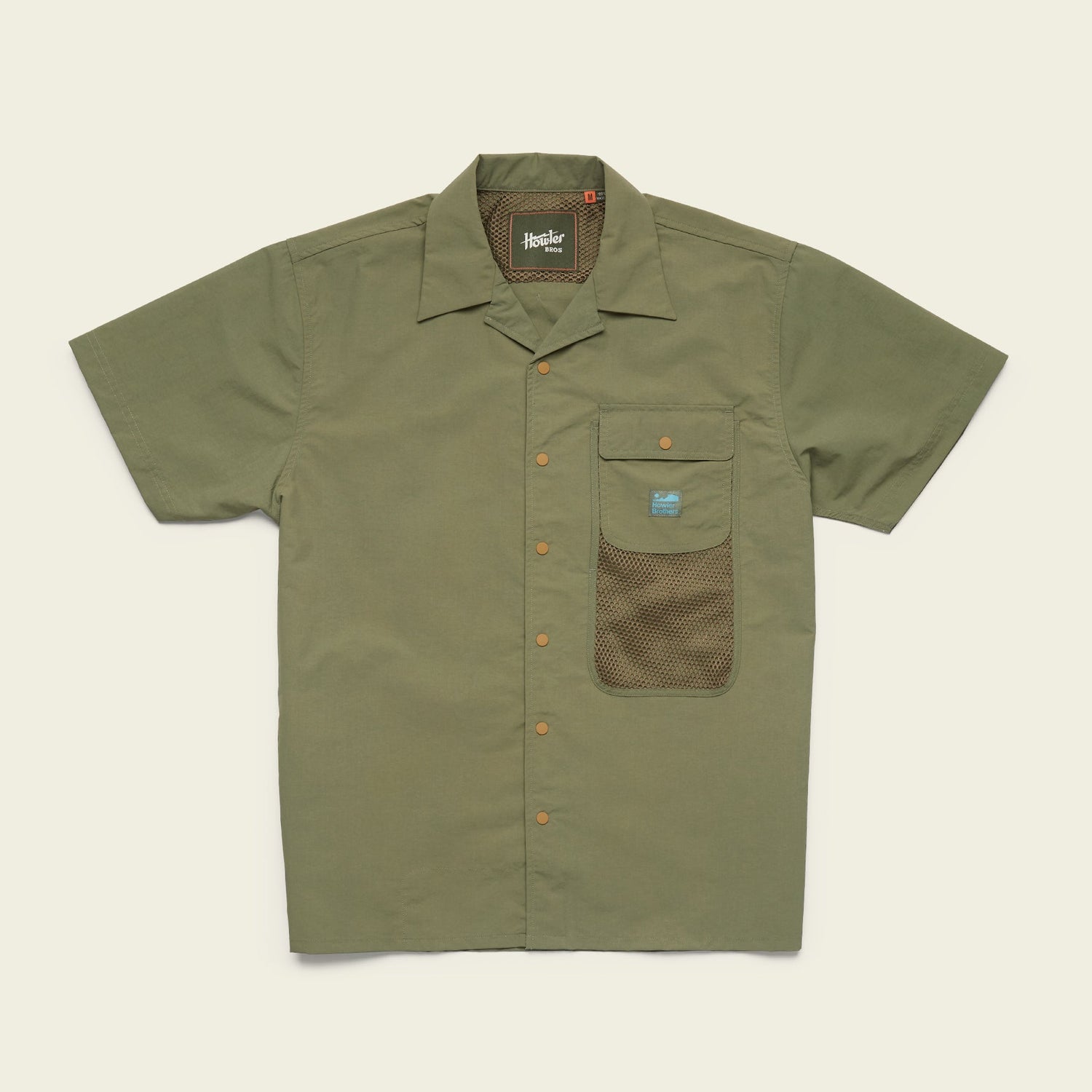 Short-sleeve olive green Forager Utility Shirt with a collar, orange buttons, and a front pocket featuring a mesh lower section and a small blue label. Perfect as a tech shirt for hiking trails. Laid flat on a light beige background.