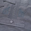 Close-up of a gray technical cotton-poly stretch fabric, showing two embroidered chevron insignias above a pocket with a button. The stitching, texture, and unique embroidery details are clearly visible.