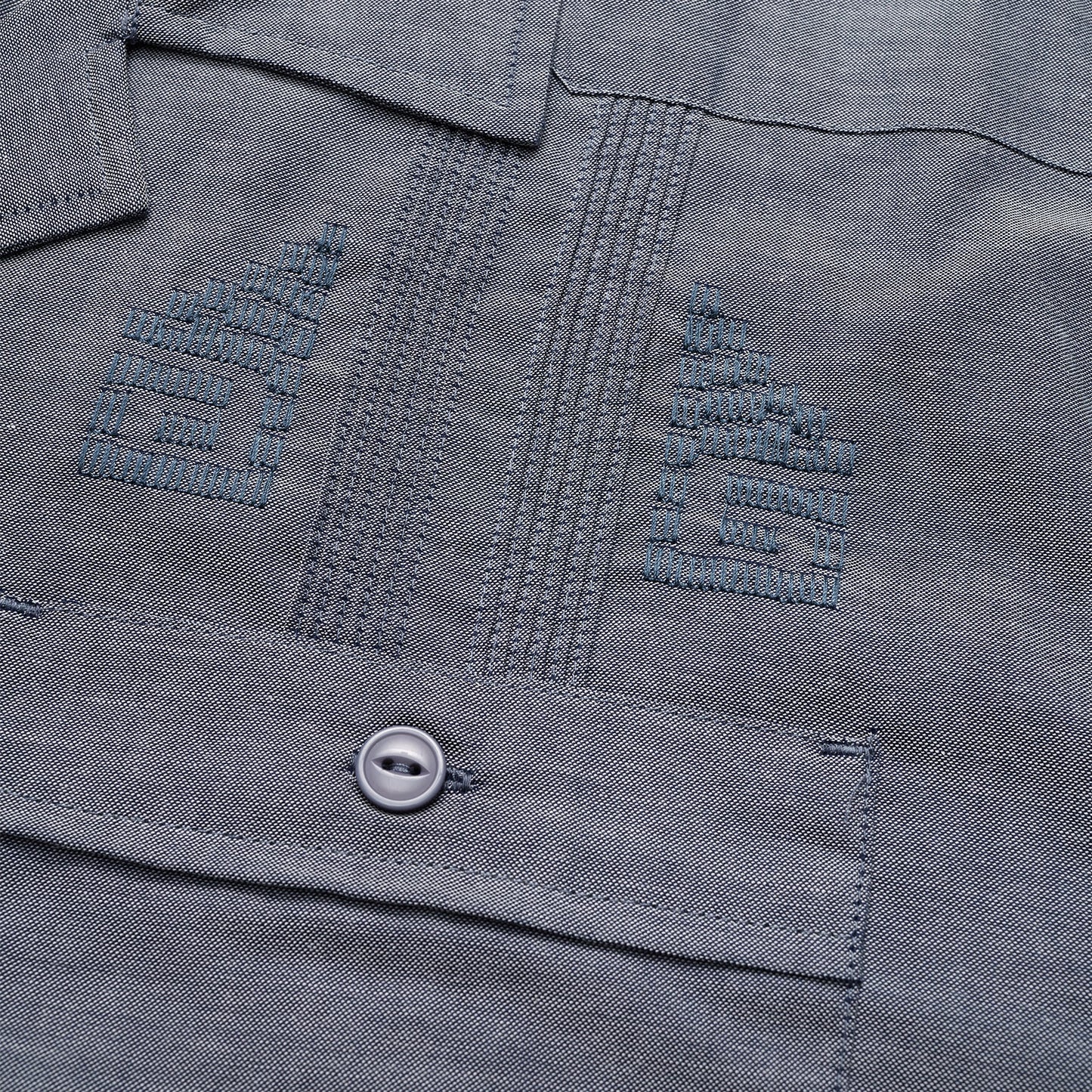 Close-up of a gray technical cotton-poly stretch fabric, showing two embroidered chevron insignias above a pocket with a button. The stitching, texture, and unique embroidery details are clearly visible.