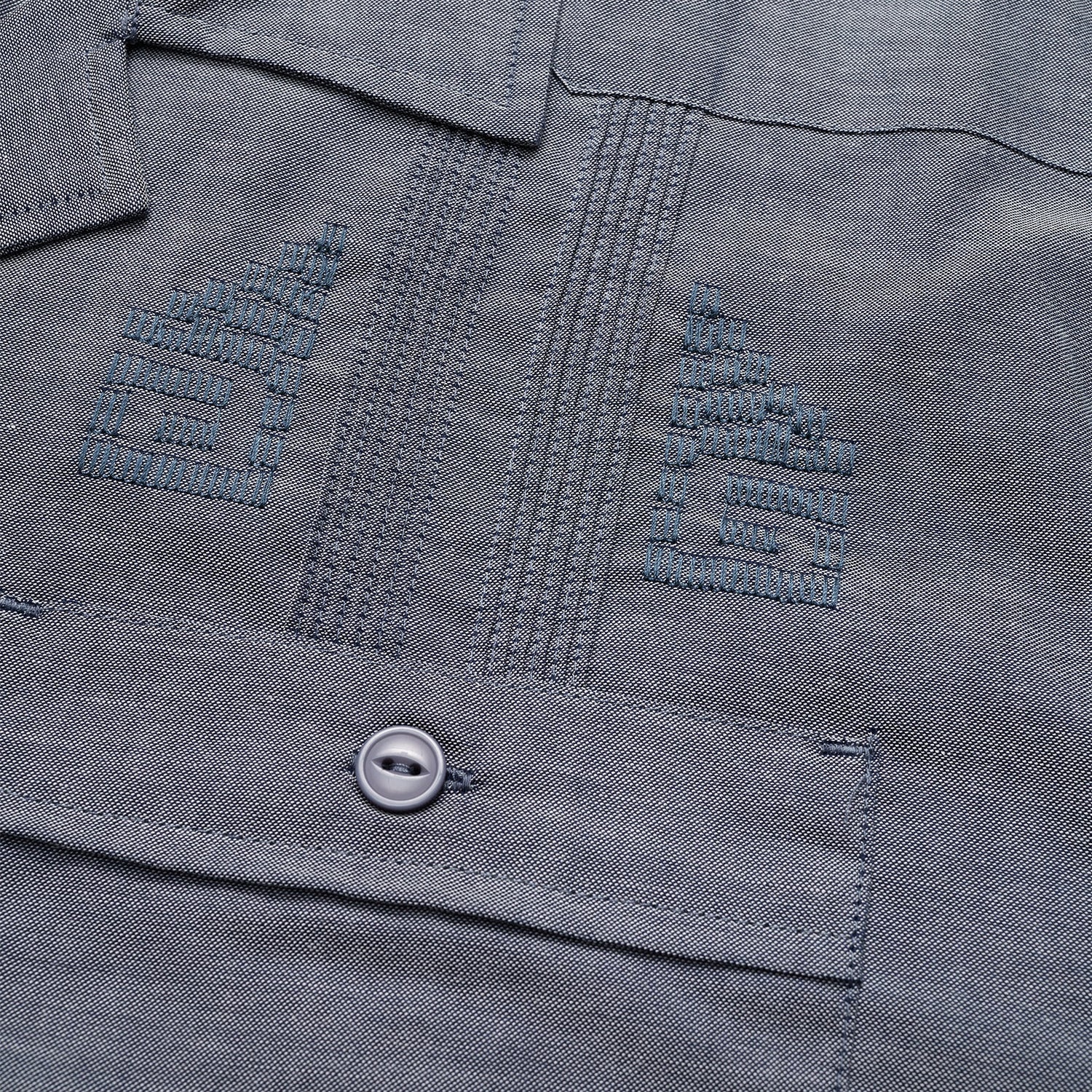 Close-up of a gray technical cotton-poly stretch fabric, showing two embroidered chevron insignias above a pocket with a button. The stitching, texture, and unique embroidery details are clearly visible.