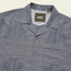 A blue short-sleeve Guayabera button-up shirt with two front pockets, unique embroidery, decorative stitching, and a Howler Bros label inside the collar.