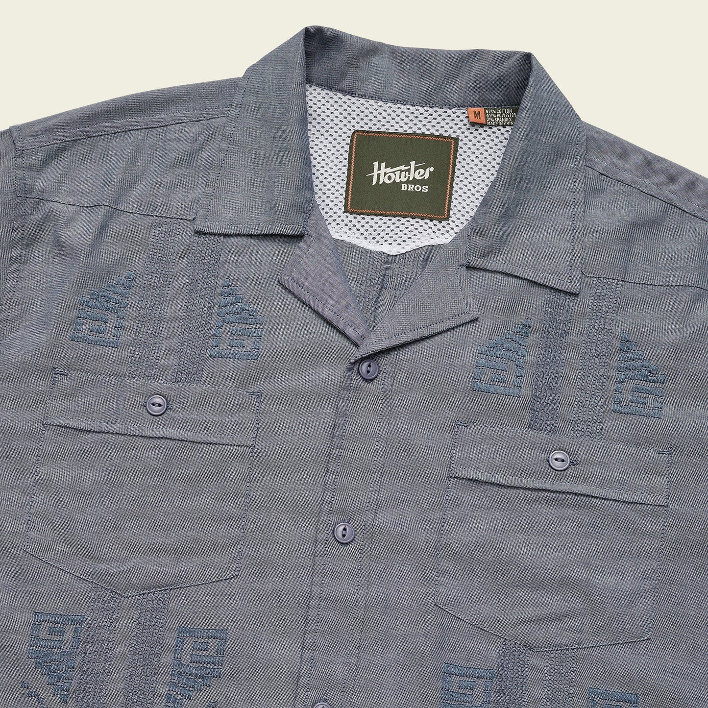 A blue short-sleeve Guayabera button-up shirt with two front pockets, unique embroidery, decorative stitching, and a Howler Bros label inside the collar.