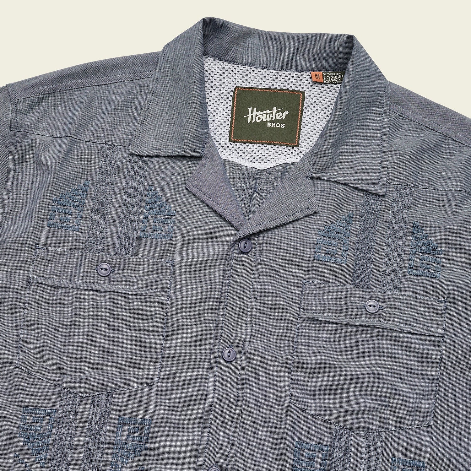 A blue short-sleeve Guayabera button-up shirt with two front pockets, unique embroidery, decorative stitching, and a Howler Bros label inside the collar.
