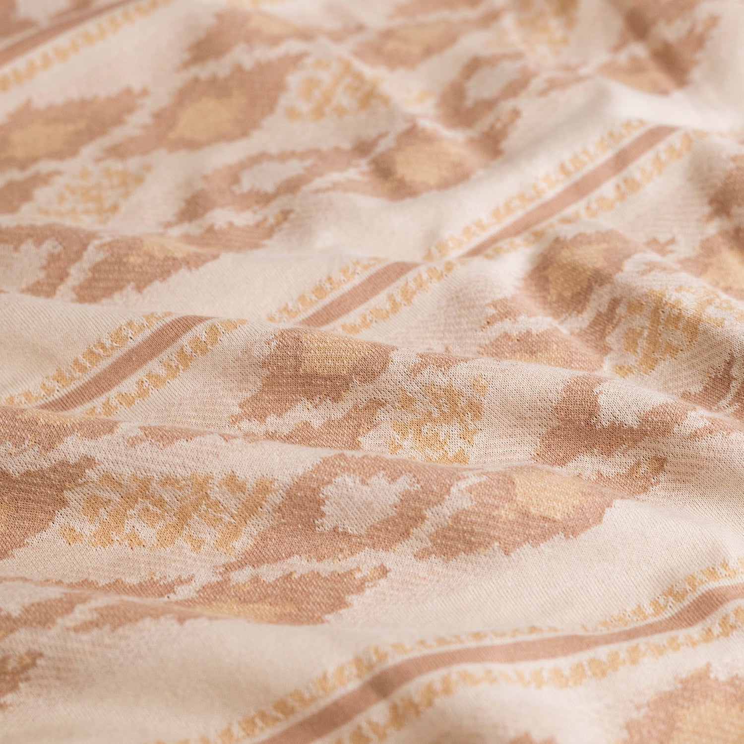 A close-up of beige and cream fabric with a woven, abstract geometric and stripe pattern in light brown and yellow tones. Made from 100% cotton jacquard, the fabric evokes the textured look of a Ranchero Jacquard Polo with soft folds.