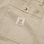 Close-up of beige cotton twill shorts featuring a front pocket with a metal button and a white label that reads “H BROS HEED THE CALL” in black text, with an orange “H” logo above it.