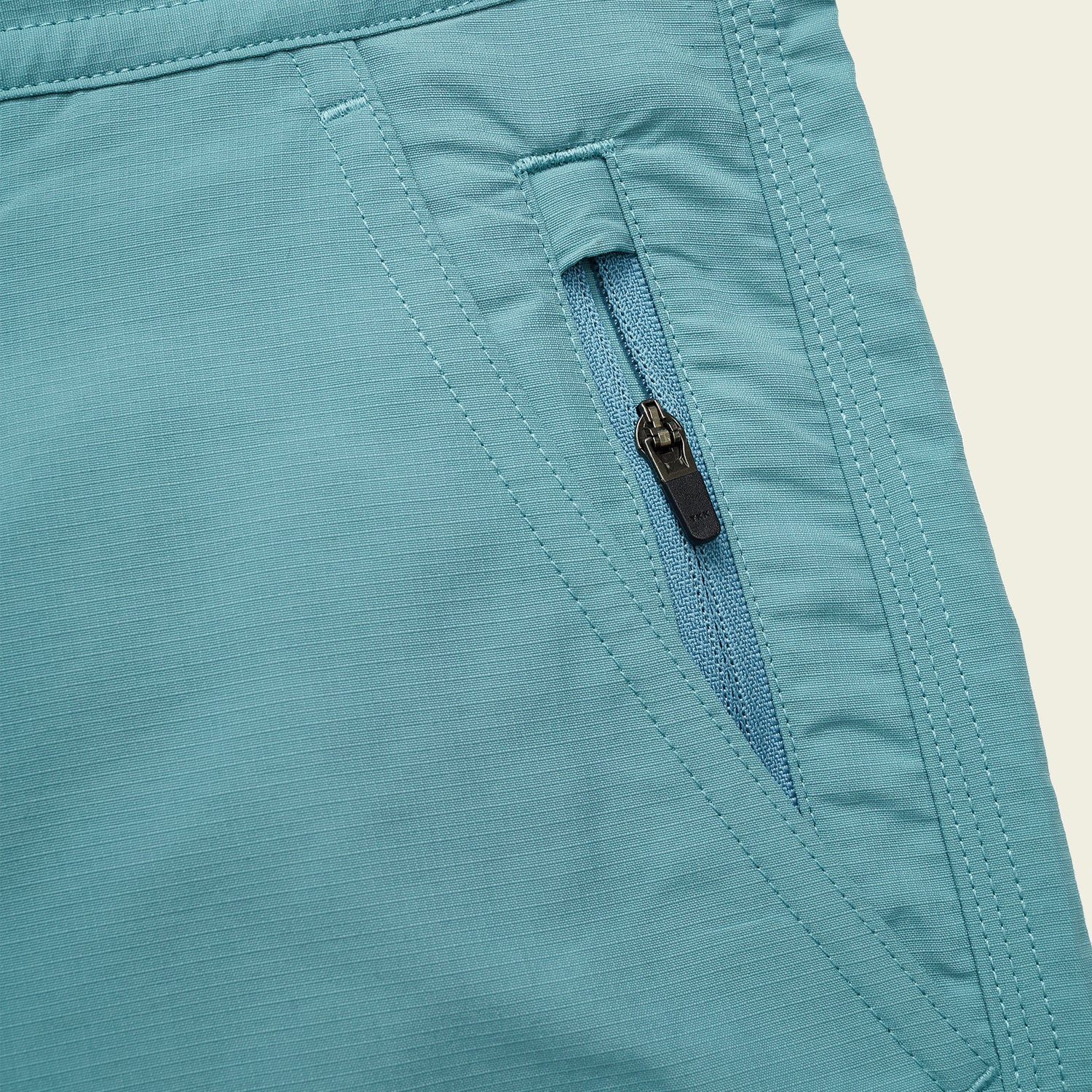 Close-up of versatile shorts, likely Horizon Hybrid Shorts, in light blue ripstop fabric, featuring a matching blue zippered pocket and visible stitching details.