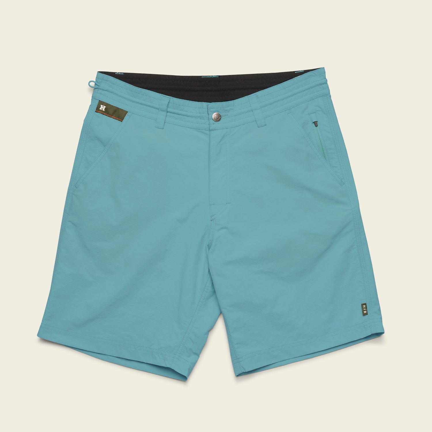 Light blue Horizon Hybrid Shorts made from durable ripstop fabric, featuring front pockets, button and zipper closure, a small black loop near the waistband, and a green patch detail on the right side. Shorts are laid flat on a light background.