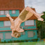 A shirtless person in Pressure Drop Cord Shorts is captured mid-backflip outdoors, with a turquoise and red building in the background. Their hair and limbs are flung outwards as they rotate, showcasing the flexibility of these comfort shorts.