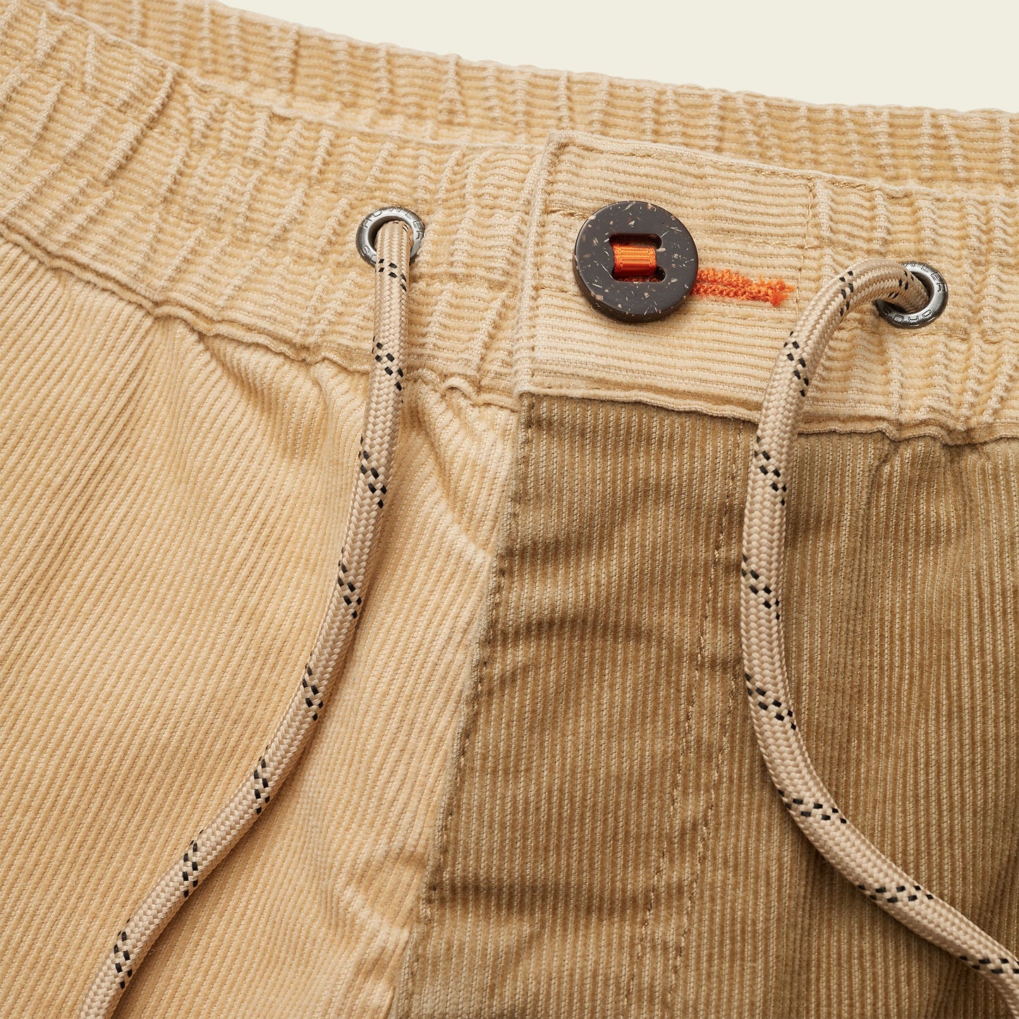 Close-up of tan Pressure Drop Cord Shorts made from stretch cotton corduroy, featuring a black button, orange stitching, an elastic waistband, and beige drawstrings with black dotted accents for all-day comfort.