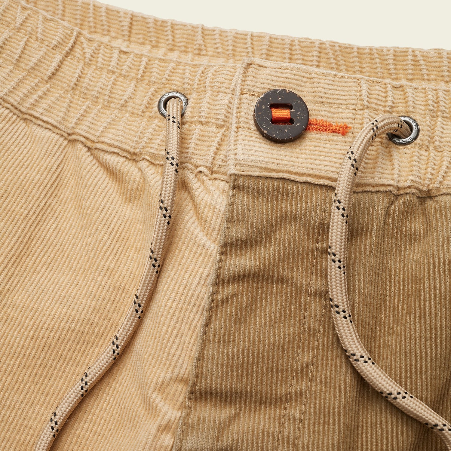 Close-up of tan Pressure Drop Cord Shorts made from stretch cotton corduroy, featuring a black button, orange stitching, an elastic waistband, and beige drawstrings with black dotted accents for all-day comfort.