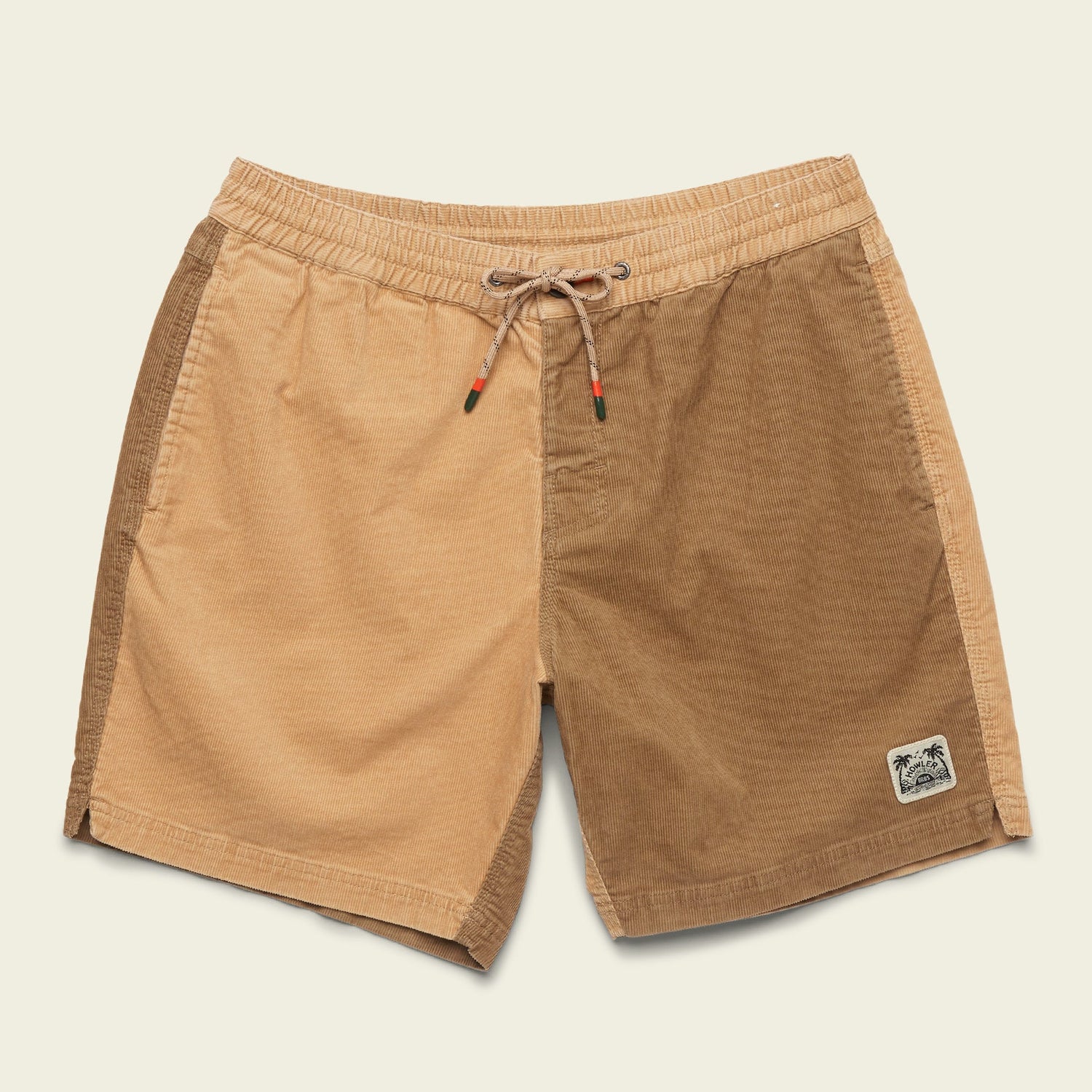 A pair of two-tone Pressure Drop Cord Shorts crafted from stretch cotton corduroy, featuring an elastic waistband, drawstring, and a small palm tree patch. The left side is light tan while the right side is a darker brown shade.