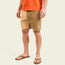 A man wearing an orange T-shirt, Pressure Drop Cord Shorts made from stretch cotton corduroy, brown flip-flops, and a ring on his left hand stands against a plain light background.