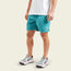 A person wearing a white t-shirt, running and hiking shorts in teal with an elastic waistband, and white sneakers with maroon and gray details, stands against a plain light background.