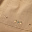 Close-up of tan cotton blend shorts with a rectangular stitched patch, featuring geometric embroidery of three acorns in green and brown. Two small metal rivets accent the edges—part of the Westside Day Shorts collection.