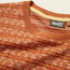 Close-up of an orange and beige patterned Howler Bros sweater, reminiscent of a vintage surf shirt, showing the collar, neck tag, and textured fabric details against a neutral background.