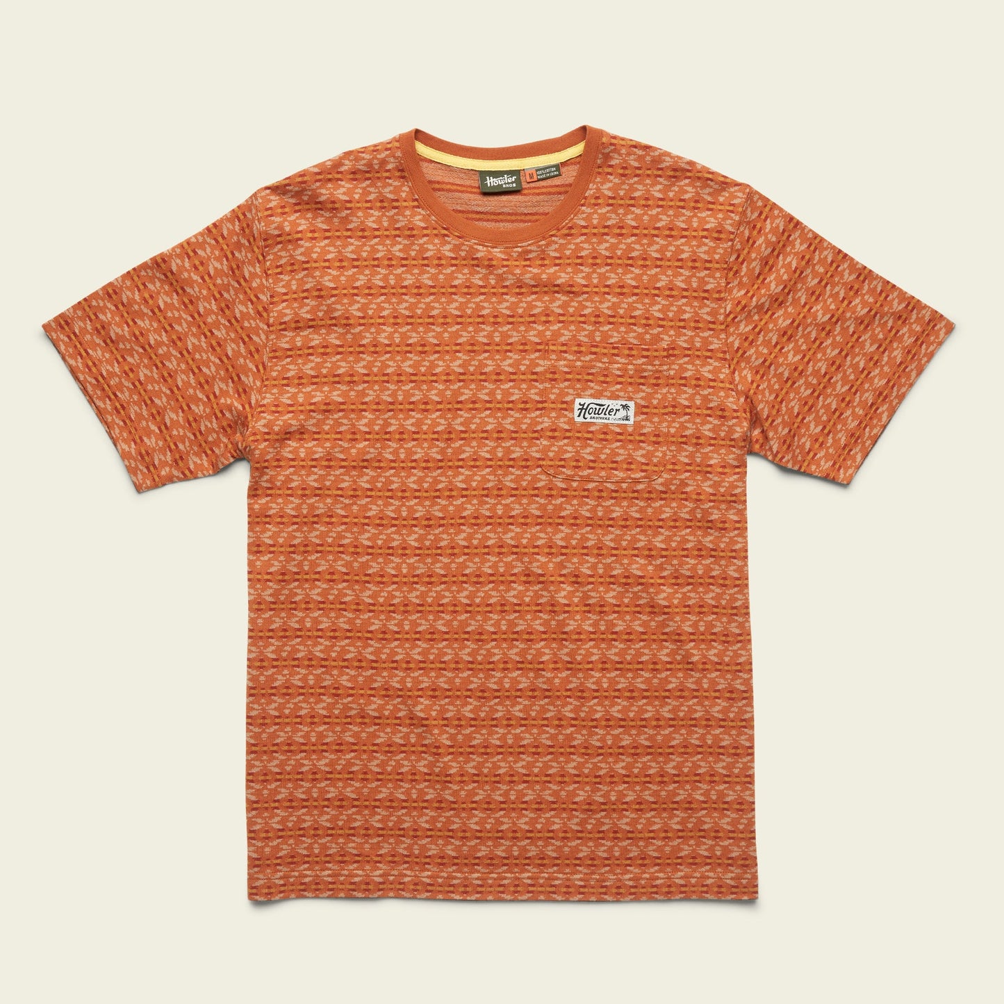 A short-sleeve orange patterned cotton jacquard t-shirt with a crew neckline and a small rectangular white patch featuring a logo on the left chest. The shirt is laid flat on a light background.