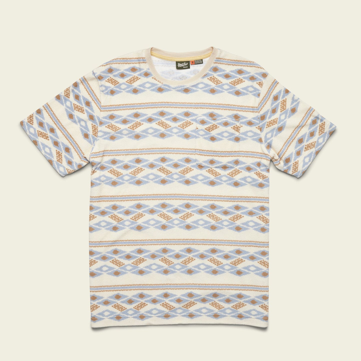 Short-sleeve T-shirt with a crew neck and an all-over geometric pattern in beige, blue, and brown tones arranged in horizontal rows. Inspired by vintage surfing t-shirts and made from comfortable terrycloth, it’s laid flat on a light background.